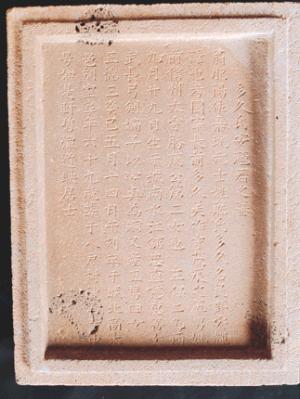 明るいベージュ色の長方形の石碑の表面に、縦書きで漢字が細かく整然と彫り込まれている多久安輝の墓誌の写真