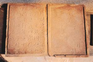 茶色く古びた石板に古い漢字の碑文が縦書きで刻まれた、見開き型の本のような形状をしている墓誌の写真