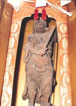 金色の装飾が施された厨子の中に安置された木造の仏像が、右手に剣を持ち左手で長い杖を突いている木彫毘沙門天立像の写真
