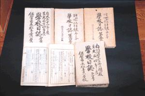 黒い背景の上に、大正時代から昭和時代初期にかけての「学校日誌」と墨書きされた複数の古い冊子が並べられ、一部は中身が開かれて当時の手書きの記録が詳細に確認できる赤松小学校の校務日誌の写真
