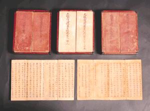 赤い箱に収められた3組の古い和綴じ本と、その手前に中身を広げた2束の古文書が並べられており、紙面には墨で書かれた多くの漢字が並んでいる様子を捉えた大興寺所蔵大般若経の写真