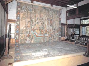 寺院の広い畳敷きの屋内に、釈迦が沙羅双樹の下で入滅する様子を大勢の弟子や動物たちが嘆き悲しむ姿で描いた、天井に届くほど巨大な「涅槃図」の掛け軸が壁一面に掲げられている様子を捉えた写真