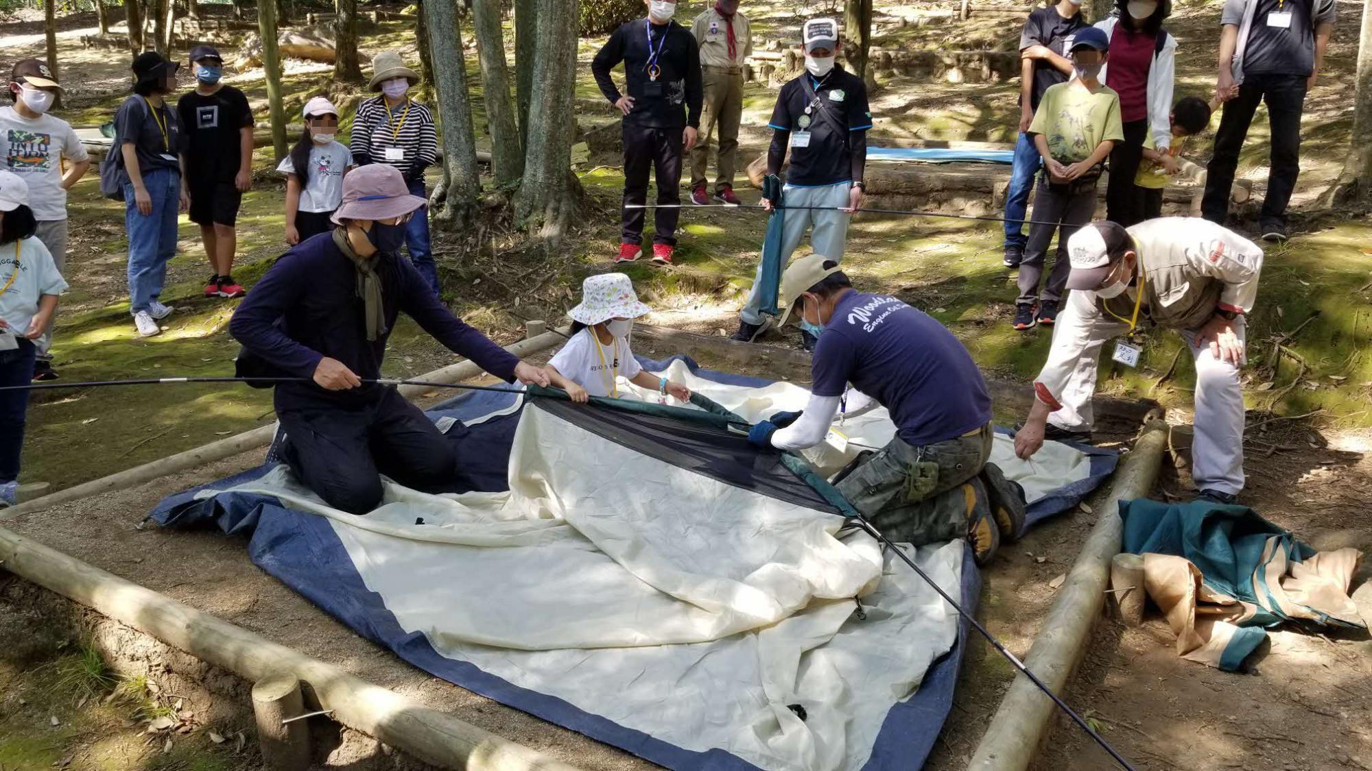 家族キャンプ体験で、指導者の説明を受けながらテントを組み立てている様子