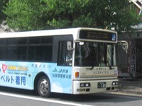 白いボディに青いラインとラッピング広告が施された路線バスが道路脇の緑豊かな街路樹の前に停車している写真