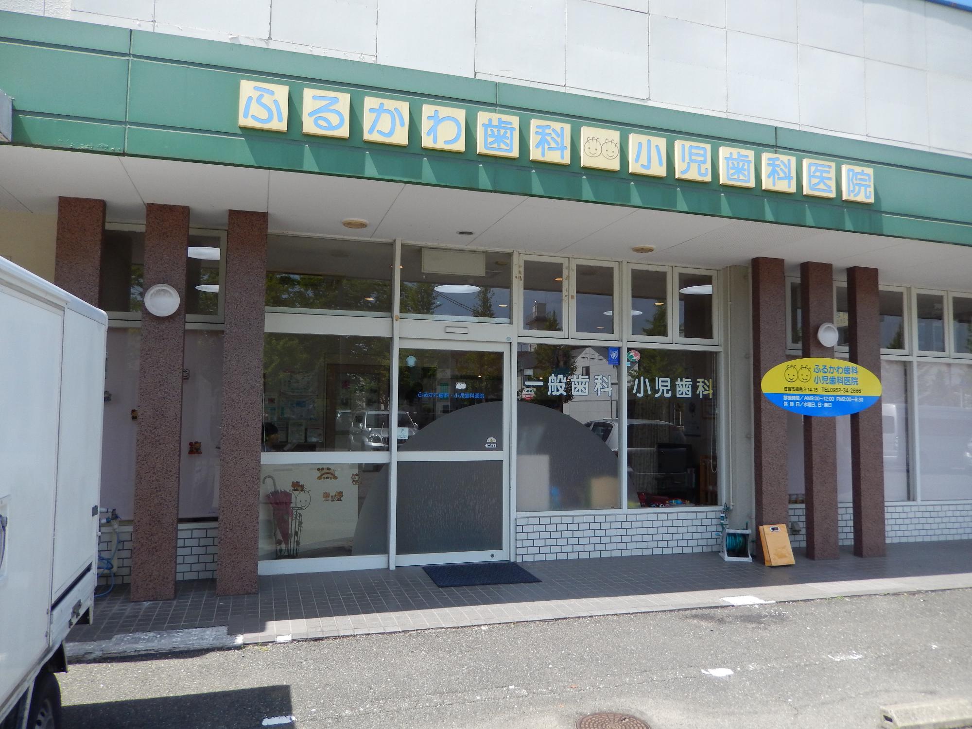 「ふるかわ歯科・小児歯科医院」と施設名が掲げられ、ガラス張りの入口には「一般歯科・小児歯科」という案内と可愛らしいキャラクター入りの楕円形看板が設置された、ふるかわ歯科医院の外観写真