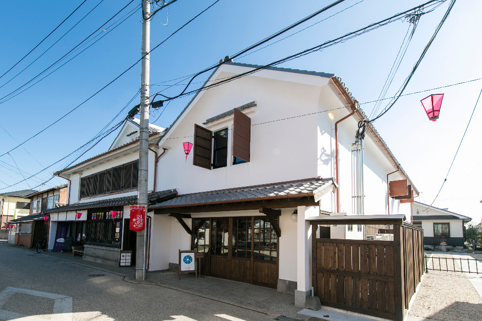 真っ白な漆喰壁と瓦屋根が美しい伝統的な蔵造りの外観を持つ二階建ての建物で、木の温もりを感じさせる格子戸の入り口や茶色の観音開き窓が配され、軒先にはピンク色の提灯が吊るされた、株式会社ハレノヒの外観写真