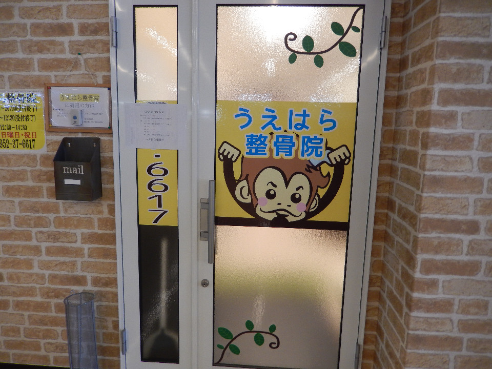 レンガ調の壁に囲まれた白い扉に、可愛らしいサルのキャラクターと共に「うえはら整骨院」という店名が大きく掲げられ、その横には電話番号の下4桁である「6617」や、診療案内が記された複数の掲示物が整然と並んでいる写真