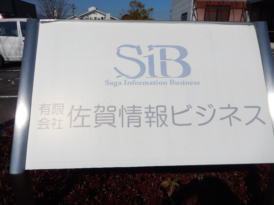 「SiB」という青いグラデーションのロゴマークと「Saga Information Business」、「有限会社 佐賀情報ビジネス」の文字で記された、屋外看板を正面から捉えた写真