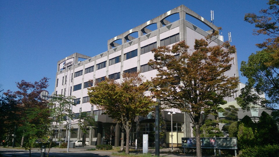 上部に「佐賀新聞社」の看板が掲げられた大きなビルが建っており、屋上部分のアーチ状の梁や整然と並ぶ窓が特徴的な多階建ての社屋を写した佐賀新聞社社屋の写真