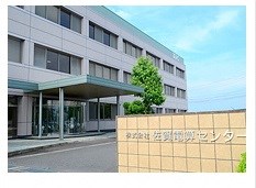 手前のベージュ色のタイル壁に「株式会社 佐賀電算センター」という社名が刻まれており、奥に3階建てのオフィスビルが建っている佐賀電算センターの写真