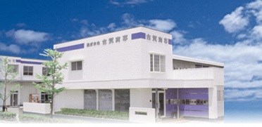 白い外壁に紫色のラインと「株式会社吉賢商事」が書かれた株式会社古賀商事の外観写真