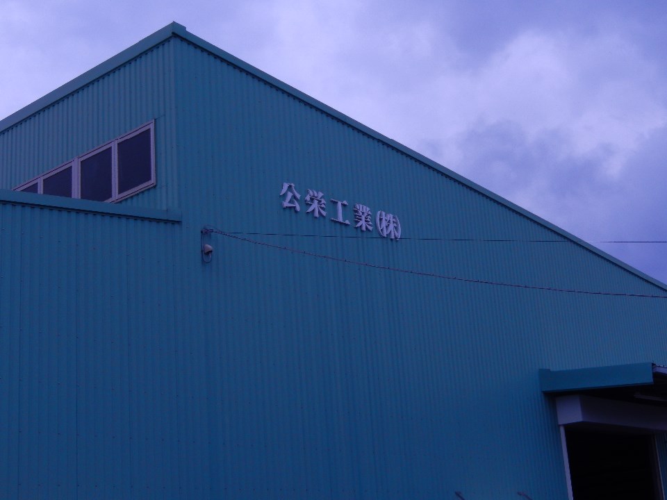 鮮やかな水色の波板スレート壁の中央に白い「公栄工業株式会社」が掲げられた外観写真