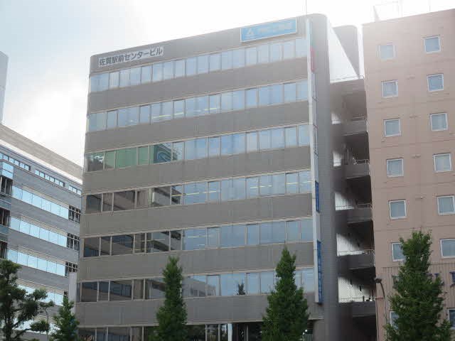最上階の壁面には「佐賀駅前センタービル」という施設名が記され、屋上付近には青い看板も設置され、落ち着いたグレーの外壁に多くの窓が整然と並ぶ多層階のオフィスビルの写真