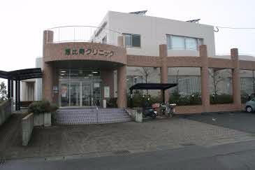 レンガ調タイルと白い外壁を組み合わせた二階建てのクリニックで、正面には「恵比寿クリニック」の文字が入った半円形のエントランスがあり、入口付近には屋根付きの駐輪スペースやスロープが設置されている建物写真