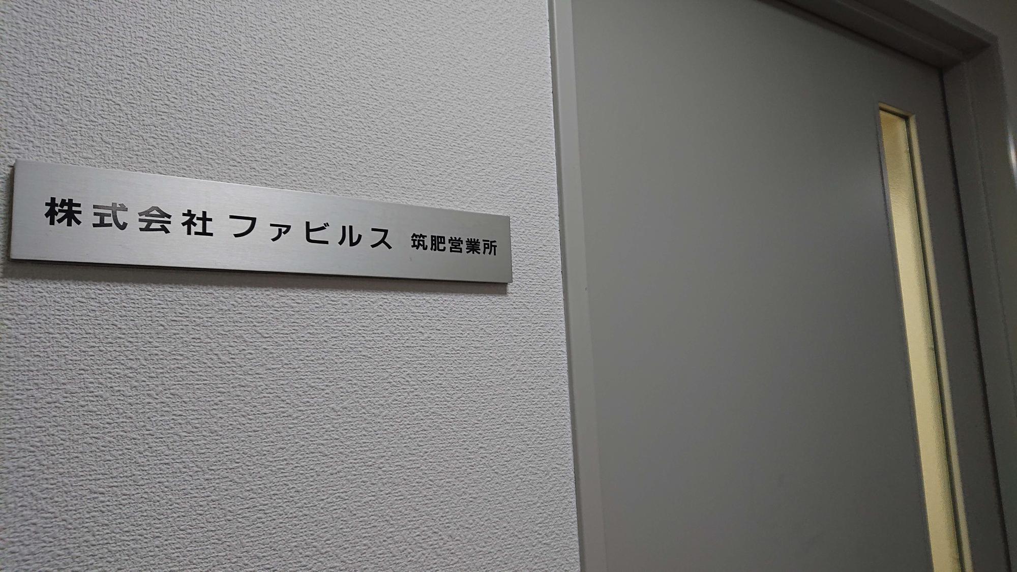 白い壁面に設置されたシルバーの銘板に、黒い文字で「株式会社 ファビルス 筑肥営業所」と営業所名が記された入り口の写真