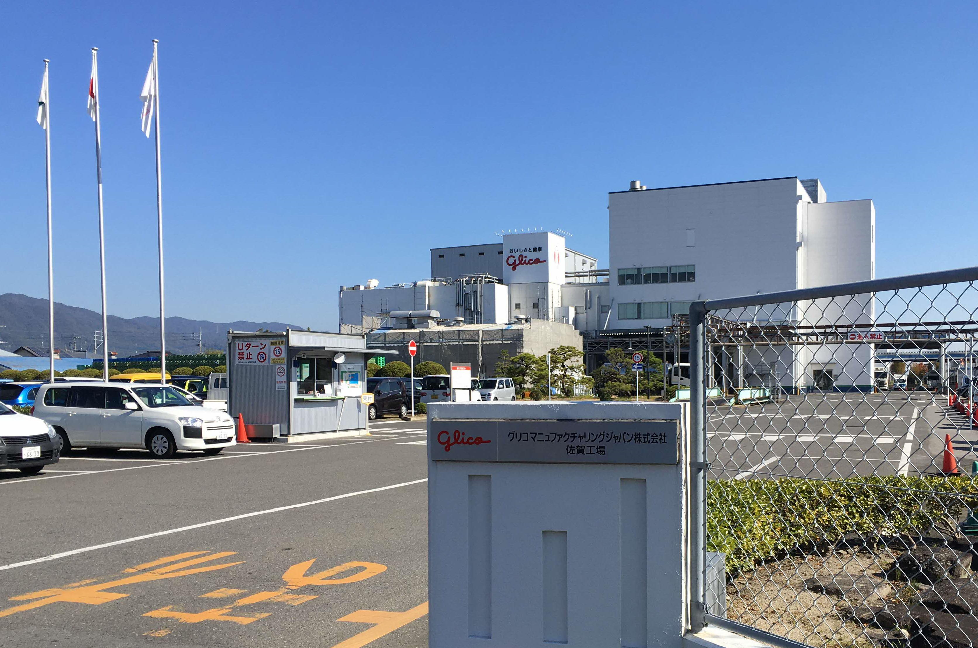 巨大な工場建屋と広大な駐車場が広がる、グリコマニュファクチャリングジャパン株式会社佐賀工場の全景写真