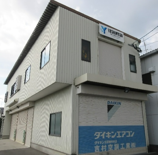 1階の大きなシャッターには「DAIKIN ダイキンエアコン 吉村空調工業株式会社」の文字が青と白で大きく描かれ、2階の搬入口の上部にも「YOSHIMURA」の社名看板が掲示された建物の写真