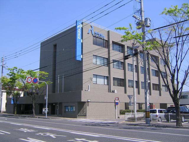 外壁がグレーのビルが建っており、青いロゴが掲げられ、ビルの角に設置された大きな青い看板には「ろうきん」の文字が記されている、街路樹の緑が映えるオフィスビルの写真