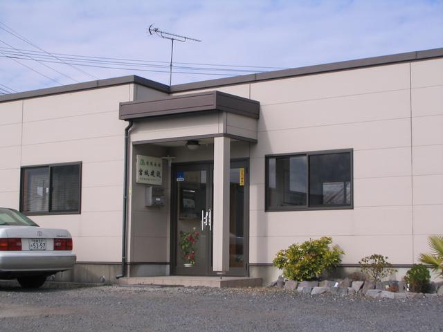 入り口横には「宮城建設」と書かれた看板が掲げられ、薄いベージュの外壁に茶色の縁取りが施された平屋建ての事務所の写真