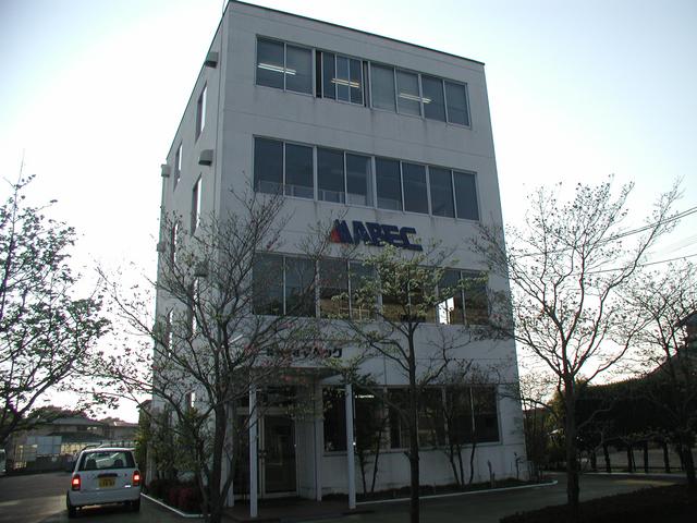 白い外壁に多くの窓が並ぶ4階建てのオフィスビルで、正面の壁面には「ABEC」という紺色の英字ロゴが大きく掲げられたマベックの建物の外観写真