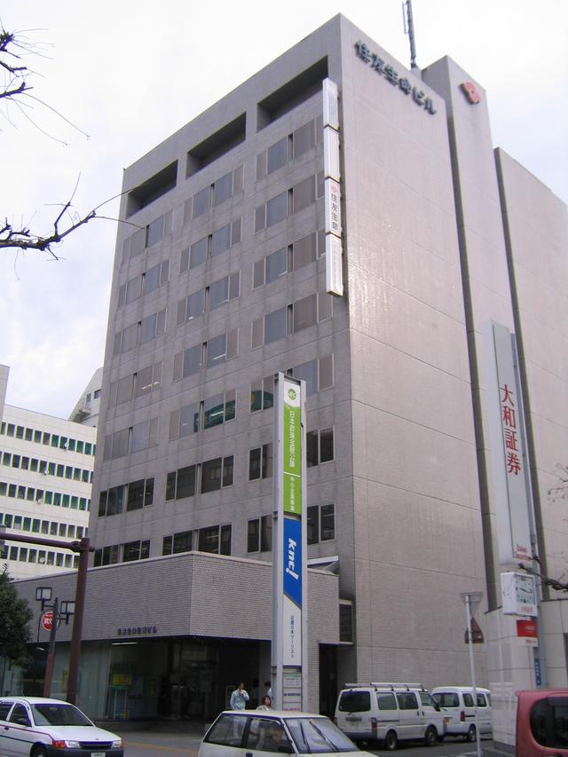 壁面に「住友生命」や「大和証券」の縦長看板が掲げられ、薄いグレーの外装が施された高層の「住友生命ビル」の外観写真