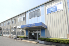 「株式会社 戸上化成」の青い庇が特徴的な工場併設の事務所ビルで、壁面には製品紹介のような大きなパネルが掲げられた株式会社 戸上化成の外観写真