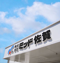 外壁部分に「株式会社 ミッド佐賀」の文字とロゴマークが大きく取り付けられている様子を斜め下から見上げた写真