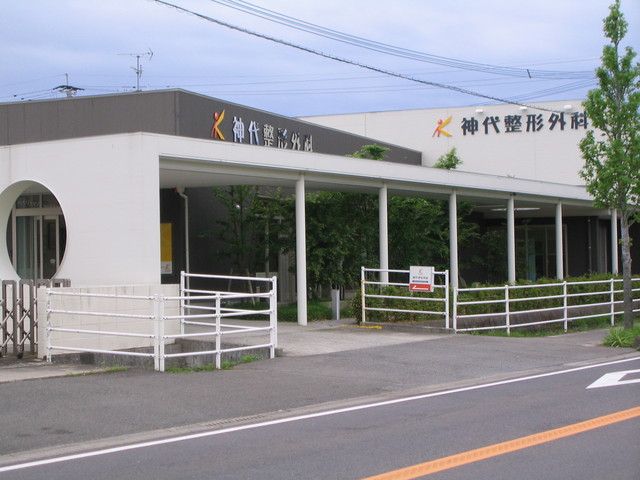平屋建ての白い外壁に丸窓が特徴的な神代整形外科の建物外観写真