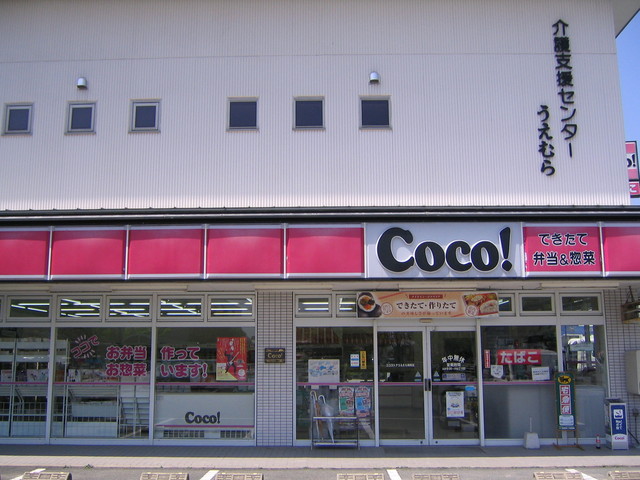 白い外壁の建物一階に赤と白の配色が目立つ「Coco!」の看板を掲げ、ガラス張りの入口やポスターが並ぶ店舗正面を撮影した写真