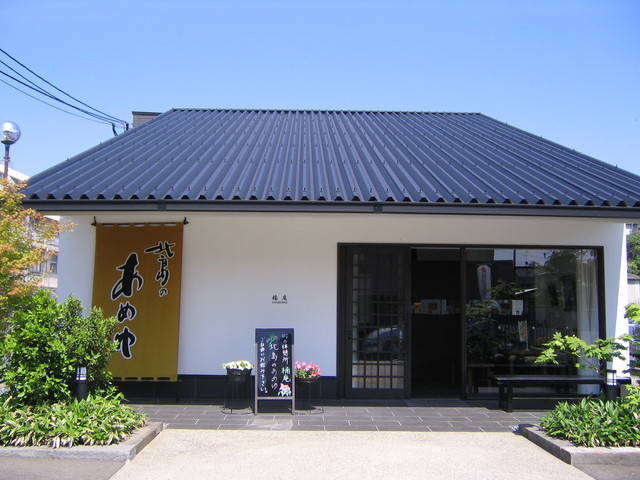 青い空の下、黒い大きな切妻屋根と白い外壁が対照的な平屋の建物で、入口横には「北島のあめゆ」と書かれた茶色の暖簾が下がり、手前にはメニュー看板や鉢植え、周囲には手入れされた緑の植栽が配置されている落ち着いた和風の店舗写真
