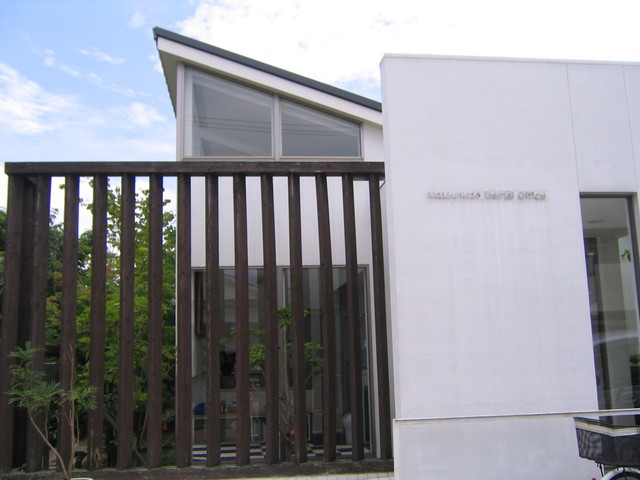 真っ白で直線的なデザインの外壁に、細長いスリット窓とシルバーのアルファベットで「Matsumoto Dental Office」と施設名が刻まれ、モダンでスタイリッシュな松本歯科医院の外観写真