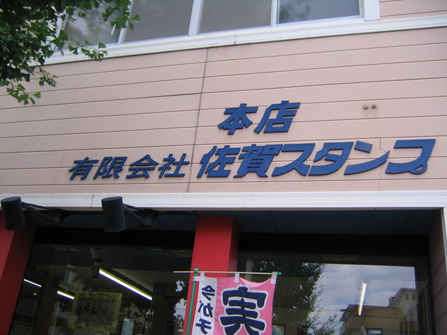 薄いピンク色の横板張りの外壁に、「本店」「有限会社 佐賀スタンプ」という紺色の大きな切り文字看板が取り付けられた有限会社佐賀スタンプの外観写真