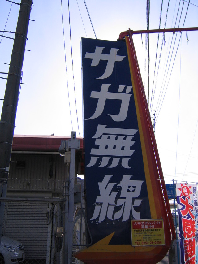 青い背景に白く大きな文字で「サガ無線」と書かれた、縦長の大きな自立式看板が設置された写真