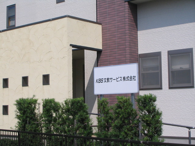 扇状の塗り壁模様が施されたベージュの外壁と落ち着いたブラウンのタイル壁が組み合わされた建物の外観写真