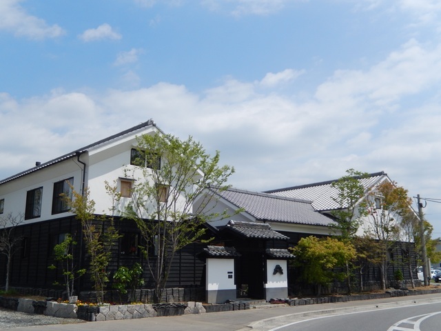 白壁の2階部分と黒い板張りの1階部分が対照的な、瓦屋根を持つ伝統的な蔵造り風の建物が2棟並んで建っているサガ電子工業株式会社の外観写真