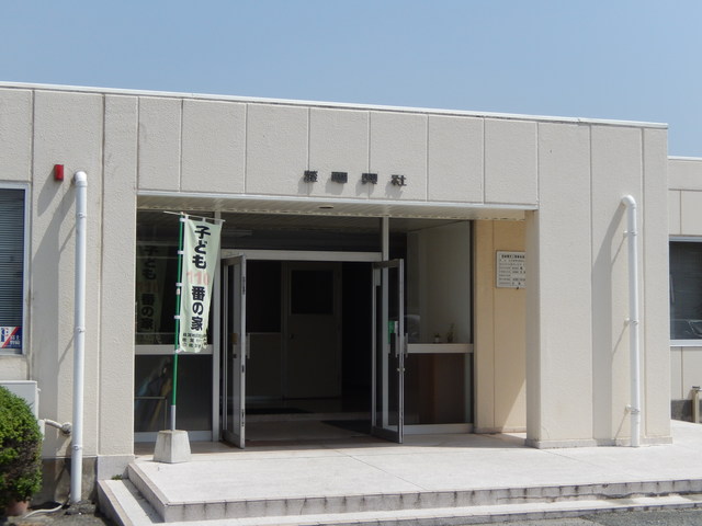 正面入口の鴨居部分には「株式会社 渡辺興社」の社名が掲げられ、玄関脇には「子ども110番の家」と書かれた緑色の旗が立つ外観写真