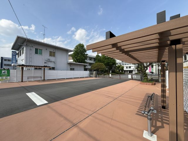 青空の下、舗装された歩道の脇に木目調のパーゴラと簡易的なベンチが設置された「SS広場」で、奥には佐賀商業高校の校舎や白いフェンスが立ち並ぶ、開放的で整然とした交流スペースを捉えた写真
