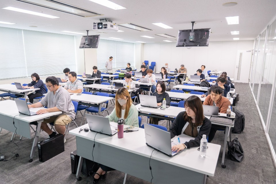 研修室で、多くの参加者が等間隔に並んだデスクに座り、各自のノートパソコンに向かって集中して作業や学習に取り組んでいるセミナーの全体風景を捉えた写真