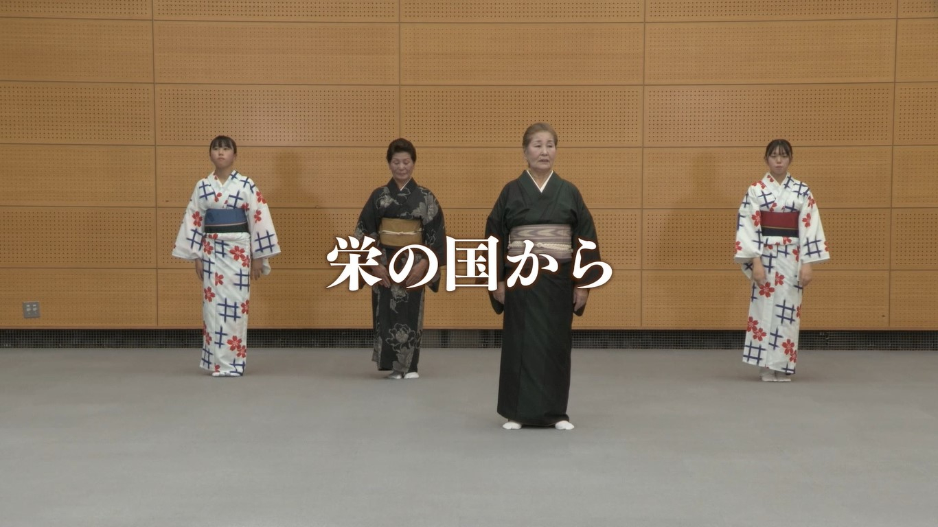 中央には大きく「栄の国から」という白い文字が重なるように配置され、木目調の壁を背景に、色とりどりの着物や浴衣を身にまとった4人の女性が等間隔に並んで立っている「栄の国から」の踊り講習映像が表示された画面キャプチャ（ 佐賀城下栄の国まつり 栄の国から 講習ビデオ（YouTube））