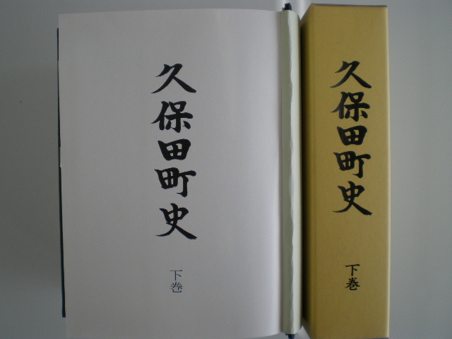 黄土色の函に久保田町史下巻と縦書きされた背表紙と、開かれた白い表紙ページに久保田町史下巻の文字が見える久保田町史(下巻)の写真