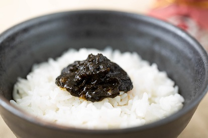 黒い茶碗に盛られた真っ白な炊きたてのご飯の上に、艶やかで濃い緑色の海苔の佃煮がこんもりと添えられた写真