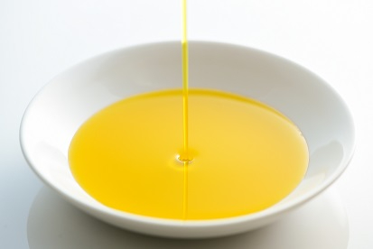 白い丸皿に、黄金色に輝く透明感のある菜種油が細い糸のように注がれている様子をとらえたイメージ写真