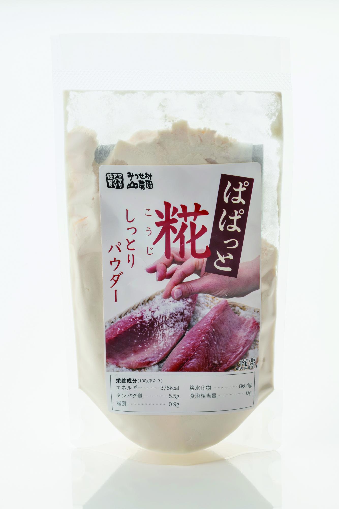 大きな赤い「糀」の文字と「ぱぱっと」というラベルに加え「しっとりパウダー」と記載され、赤身魚に粉末を振りかける調理風景が描かれた、白い粉末が詰まった透明な自立式パウチ容器の商品の写真