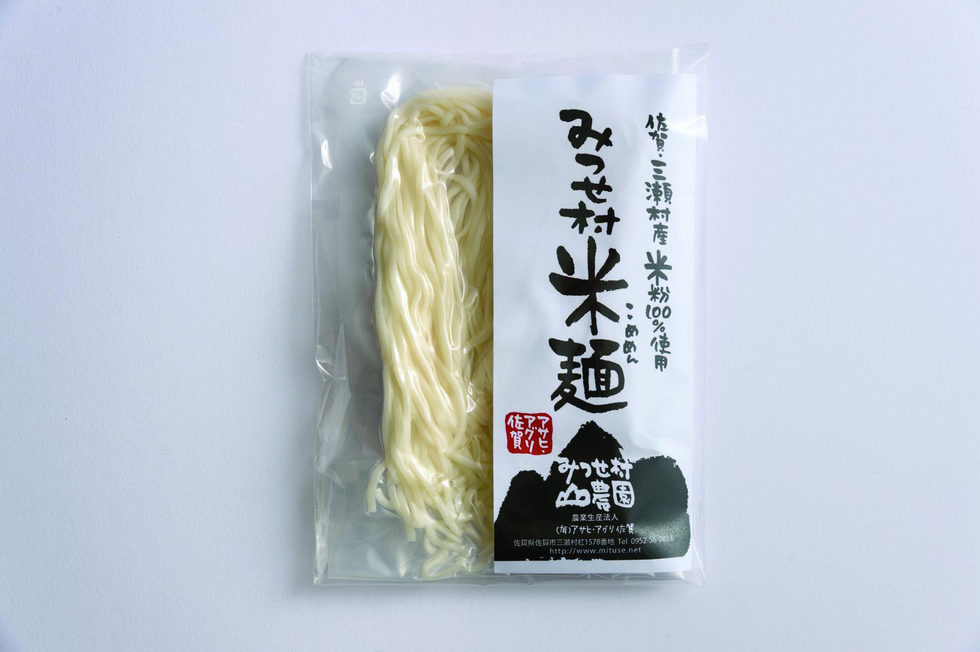 右側に「みつせ村 米麺（こめめん）」という大きな墨文字と山のようなロゴがデザインされた白いラベルが貼られ、左側の透明な袋越しに淡いクリーム色の生麺が見える、佐賀・三瀬村産の米粉100%使用した麺商品の写真