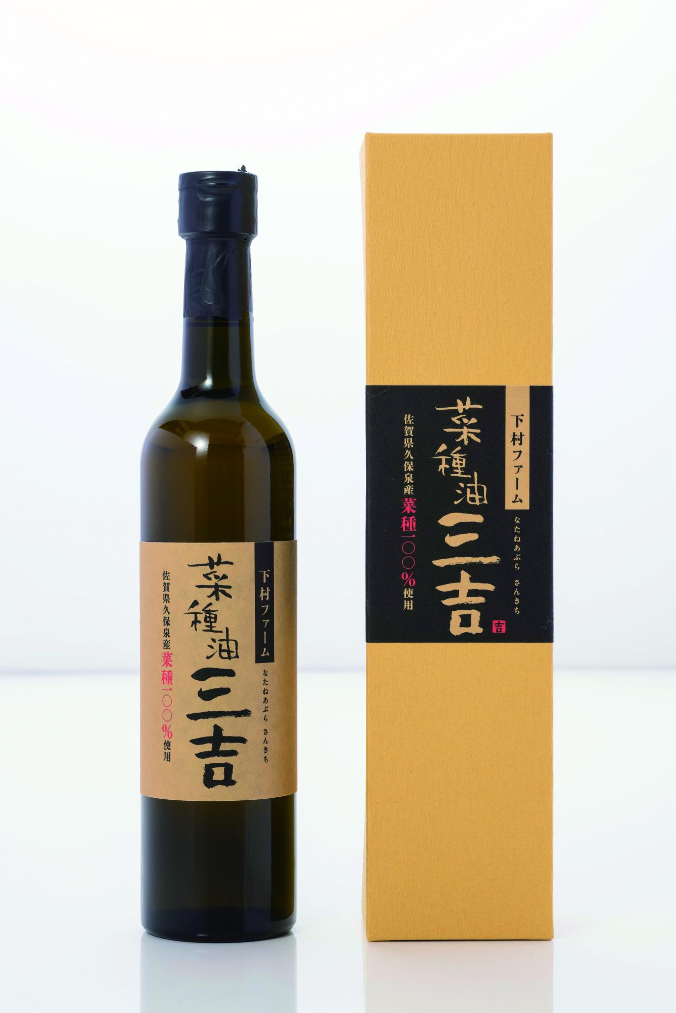 左側に「菜種油 三吉（さんきち）」という墨文字のラベルが貼られた濃い緑色のガラスボトル、右側に同様のデザインが施された山吹色の化粧箱が並んだ、下村ファームの菜種油100%使用の菜種油 三吉商品の写真