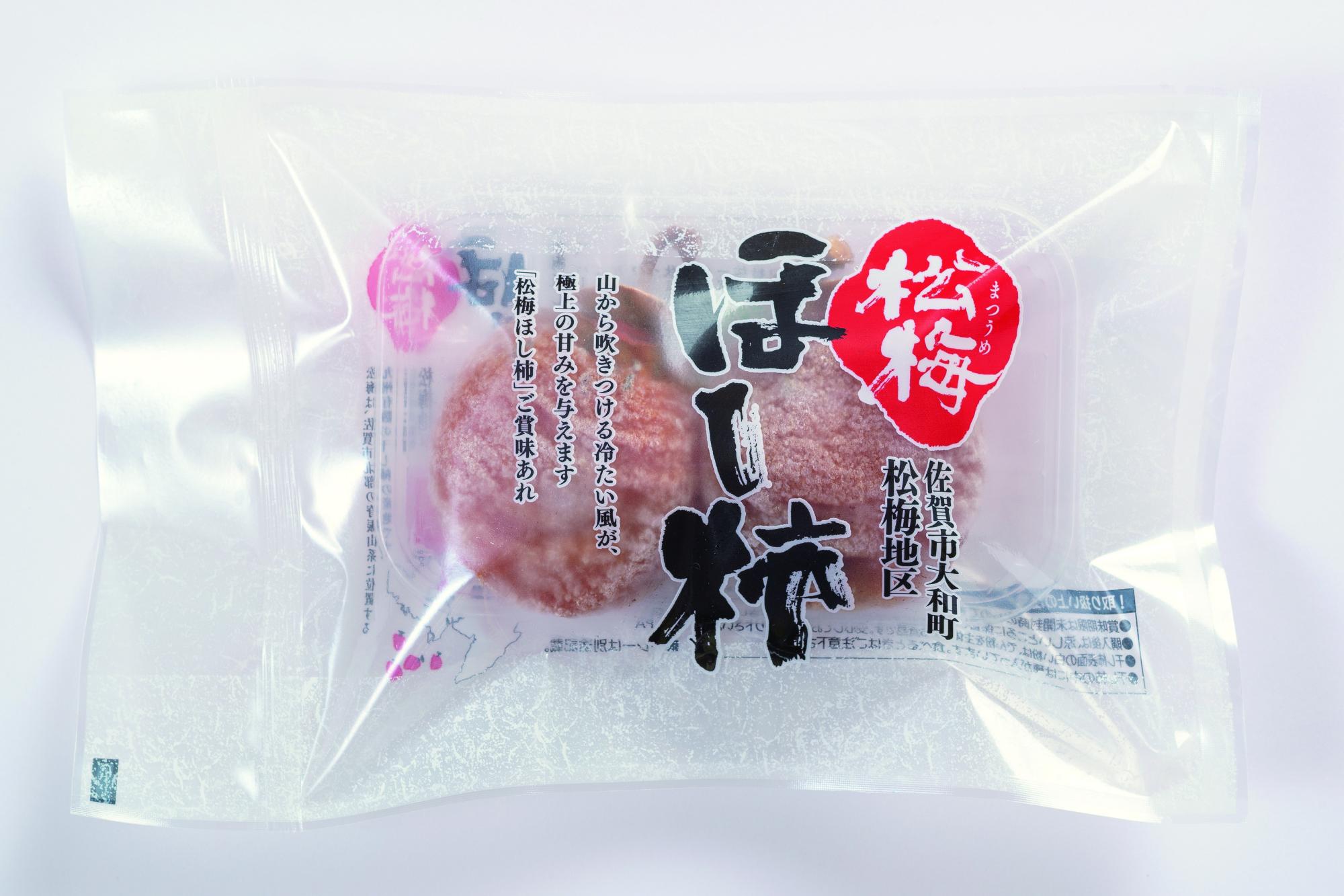 冷凍された2粒のほし柿が透けて見える透明な袋が置かれ、中央に「ほし柿」、右上に赤地に白抜きで「松梅」と力強く印字されたパッケージの商品の写真