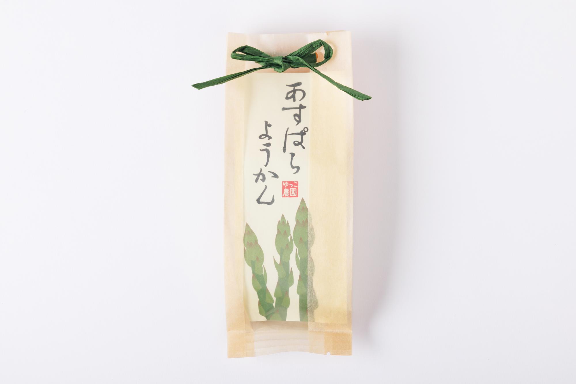 半透明の和紙のような袋に、鮮やかな緑色のアスパラガスのイラストと、柔らかな墨文字で「あすぱらようかん」と記されたラベルが貼られ、上部を緑色の紐でリボン結びにした、上品で可愛らしい和菓子の商品の写真