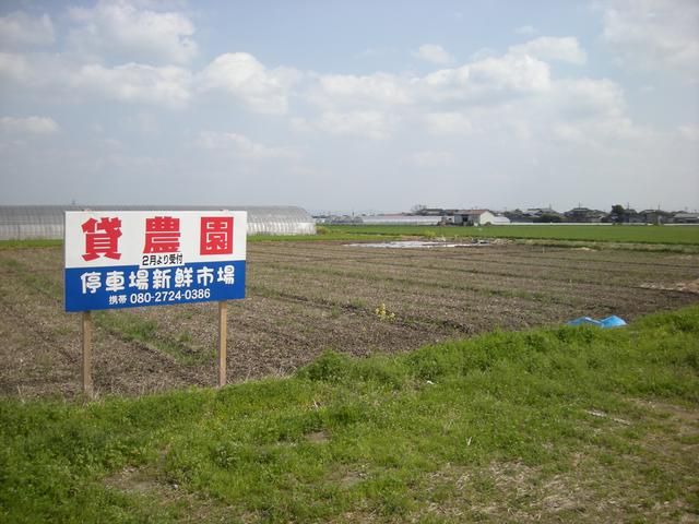 手前に緑の草地が広がり、その先に「貸農園」と書かれた大きな看板が立つ広大な農地がある停車場農園の写真