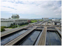 曇り空の下、建物と緑地を背景に、複数の長方形の水処理槽が並ぶ下水処理施設の写真