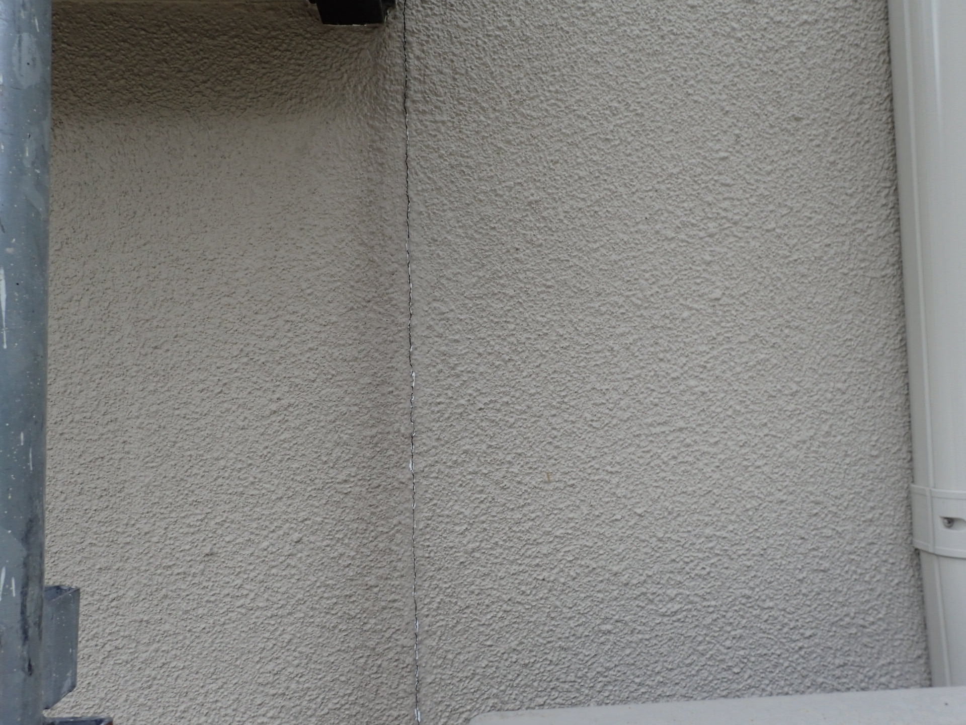 住宅外壁のざらついた塗装面を縦に細い亀裂が走っている写真